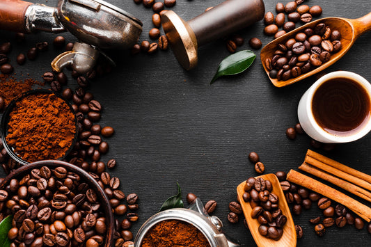 Chicchi di caffè tostati, macinino e cucchiai di legno su fondo scuro: la storia del caffè