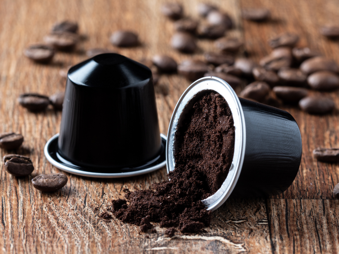 Capsule di caffè nere compatibili circondate da chicchi tostati su un tavolo di legno